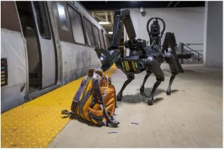 A four legged robotic device in a simulated scenario of investigating a backpack on a subway.