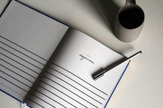 Open notebook that reads "Agenda on left page", lined paper. Coffe cup in upper right corner.