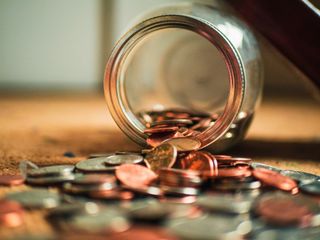 A glass jar on it's side with change spilled out onto a table.