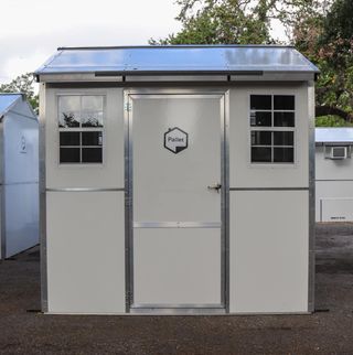A white fabricated shed with a door and two small windows flanking it.
