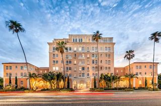 Front view of the Mirasol Apartments on Davis Blvd. A pale pink Mediterranean revival building on a palm tree lined street.