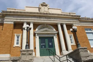 Yellow brick building facade with white columns and arched entrance. Above entrance engraved words "Free Library".